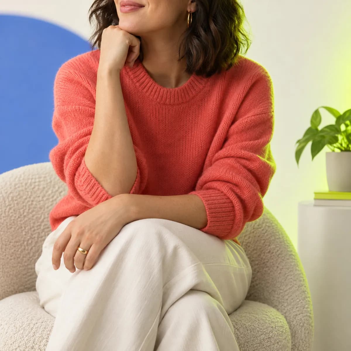 Cropped creative professional in a coral sweater against a pale studio wall