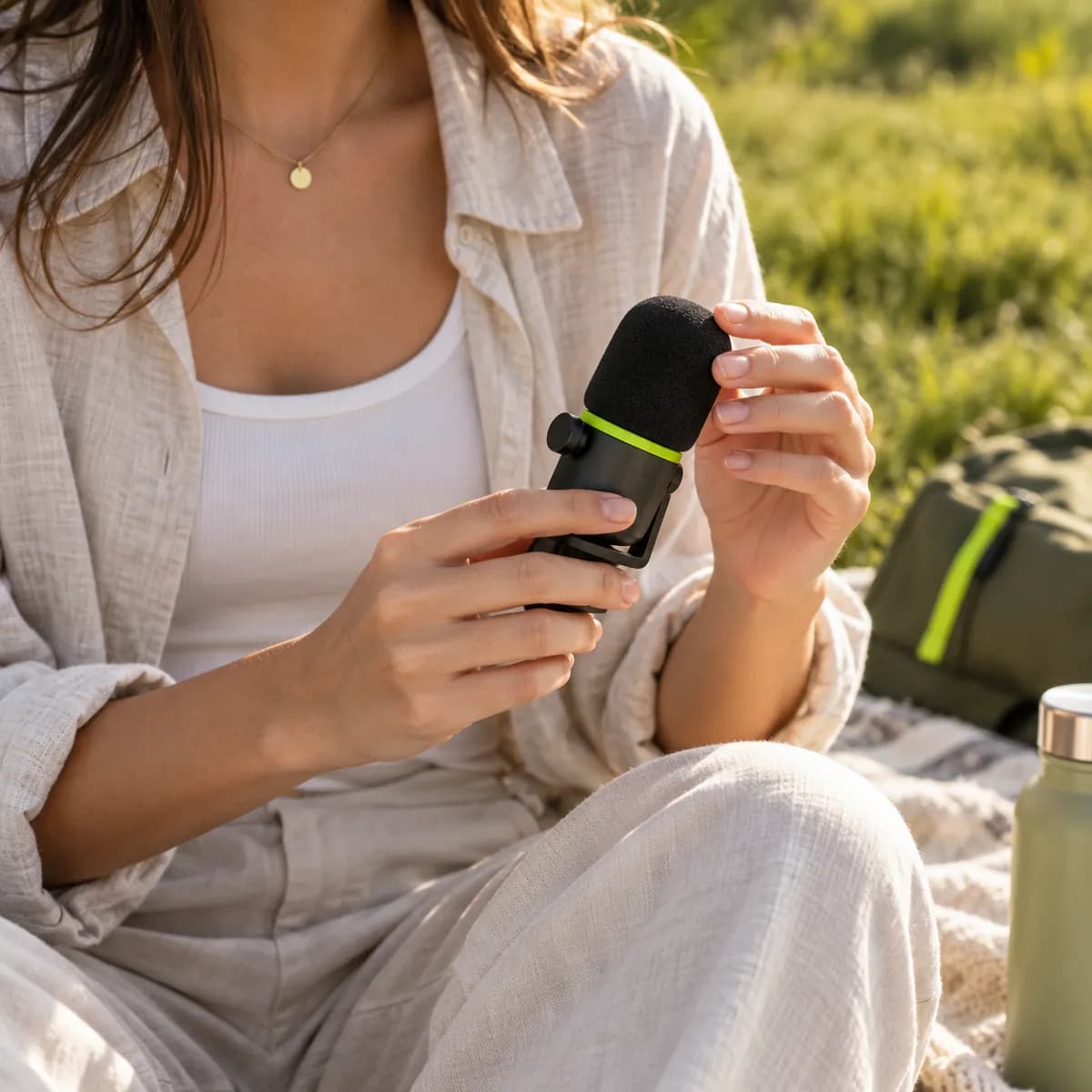 Torso-level creator recording outdoors with a handheld microphone in a warm natural setting