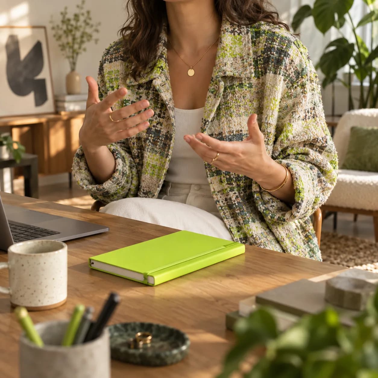 Warm editorial studio scene with a creator's hands and colorful wardrobe beside a lime notebook